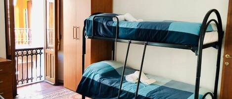 Una cama individual superpuesta con colcha azul y blanca, un armario de madera y suelo estampado.