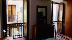 A hotel room with a bed, a desk, a chair, a mirror, and a balcony with a metal railing.