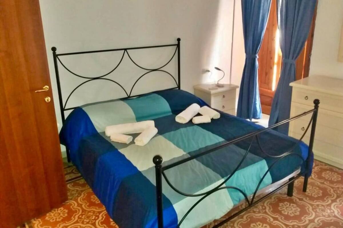 Una cama con estructura de metal, colcha a cuadros azul y verde, y toallas enrolladas sobre la cama.