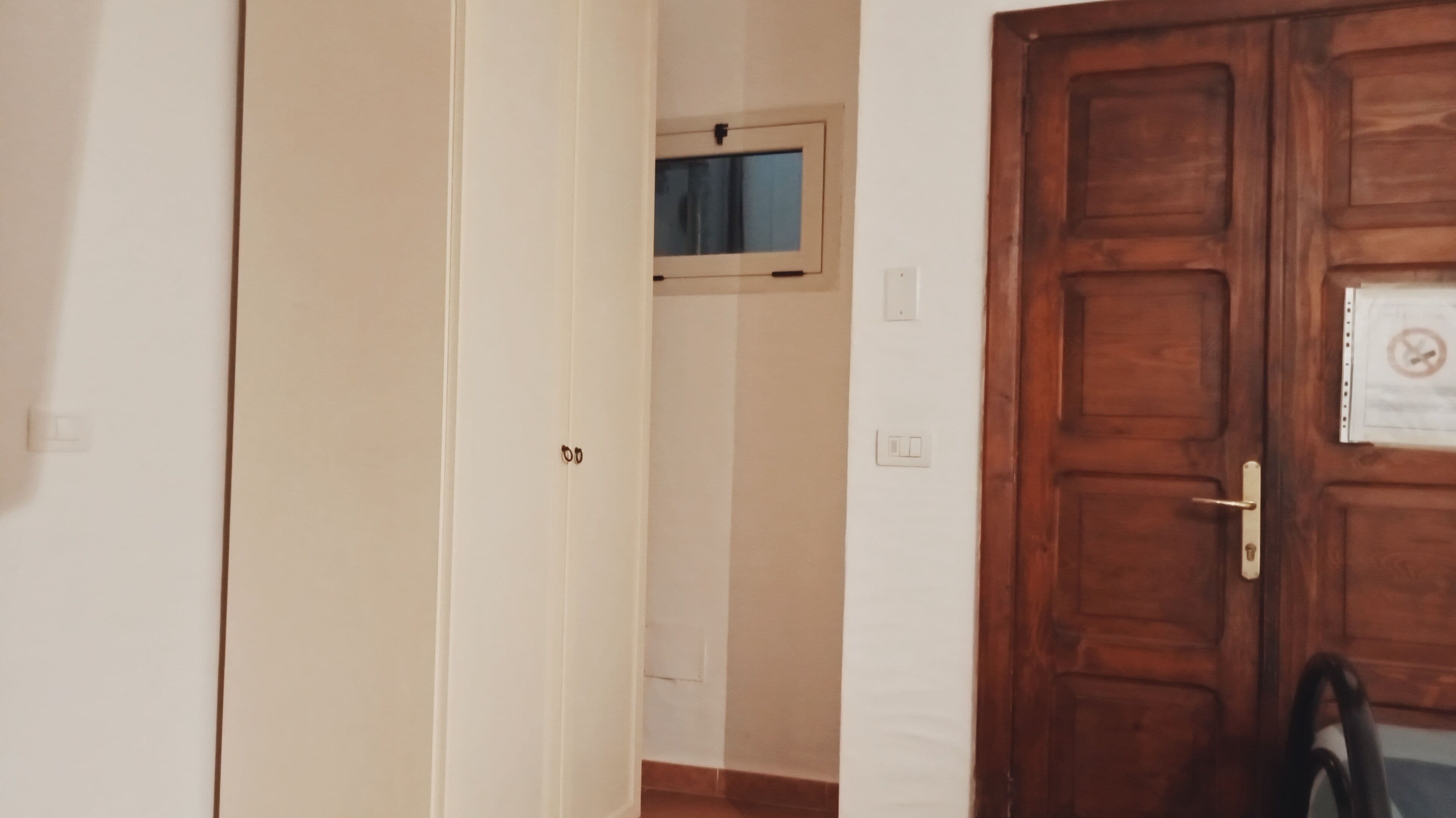 A hallway with a wooden door, a window, and a doorbell.
