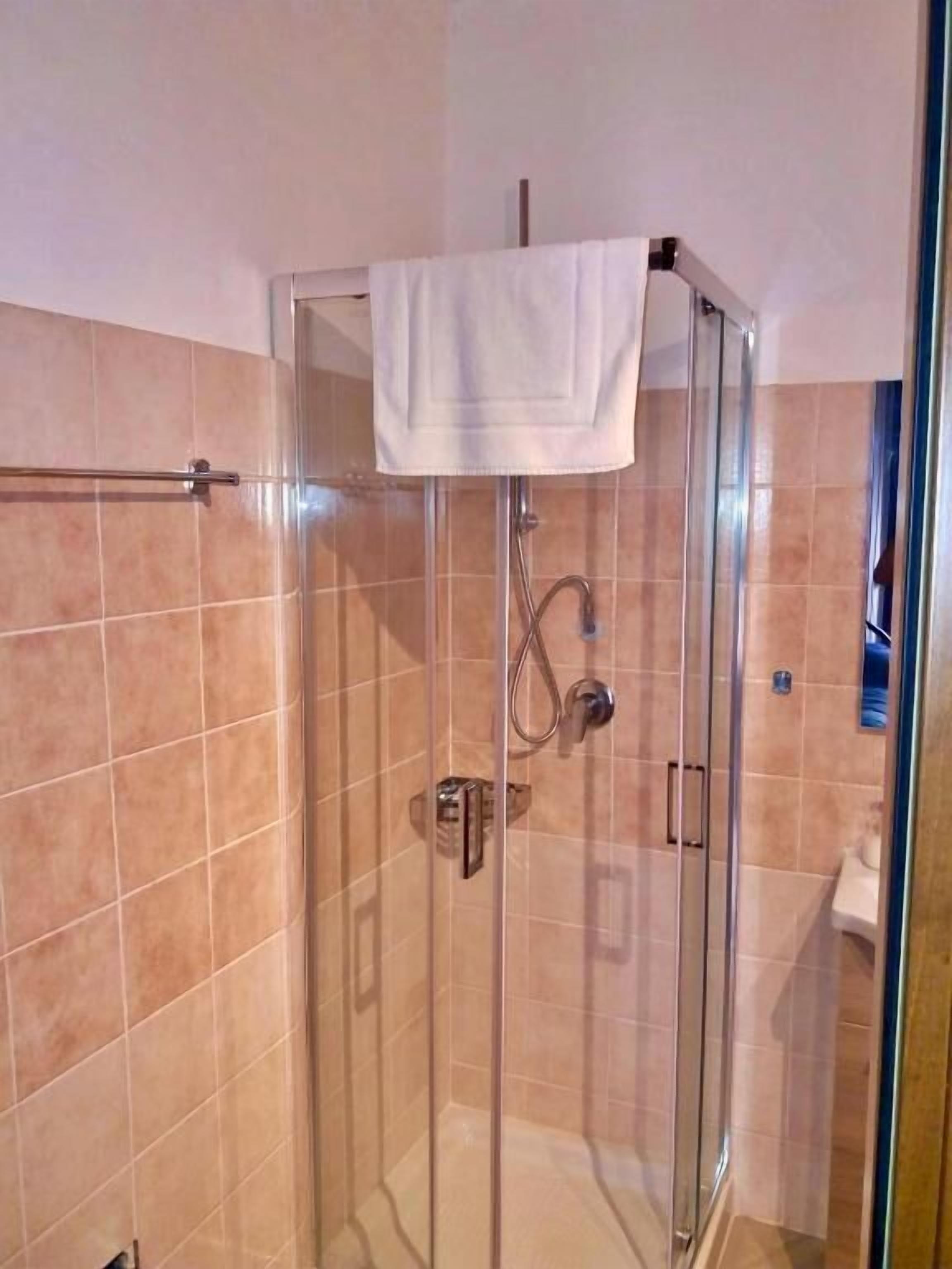 Eine gläserne Dusche mit einem am Türgriff hängenden Handtuch, einer Duschbrause und einem Handbrauseinsatz.
