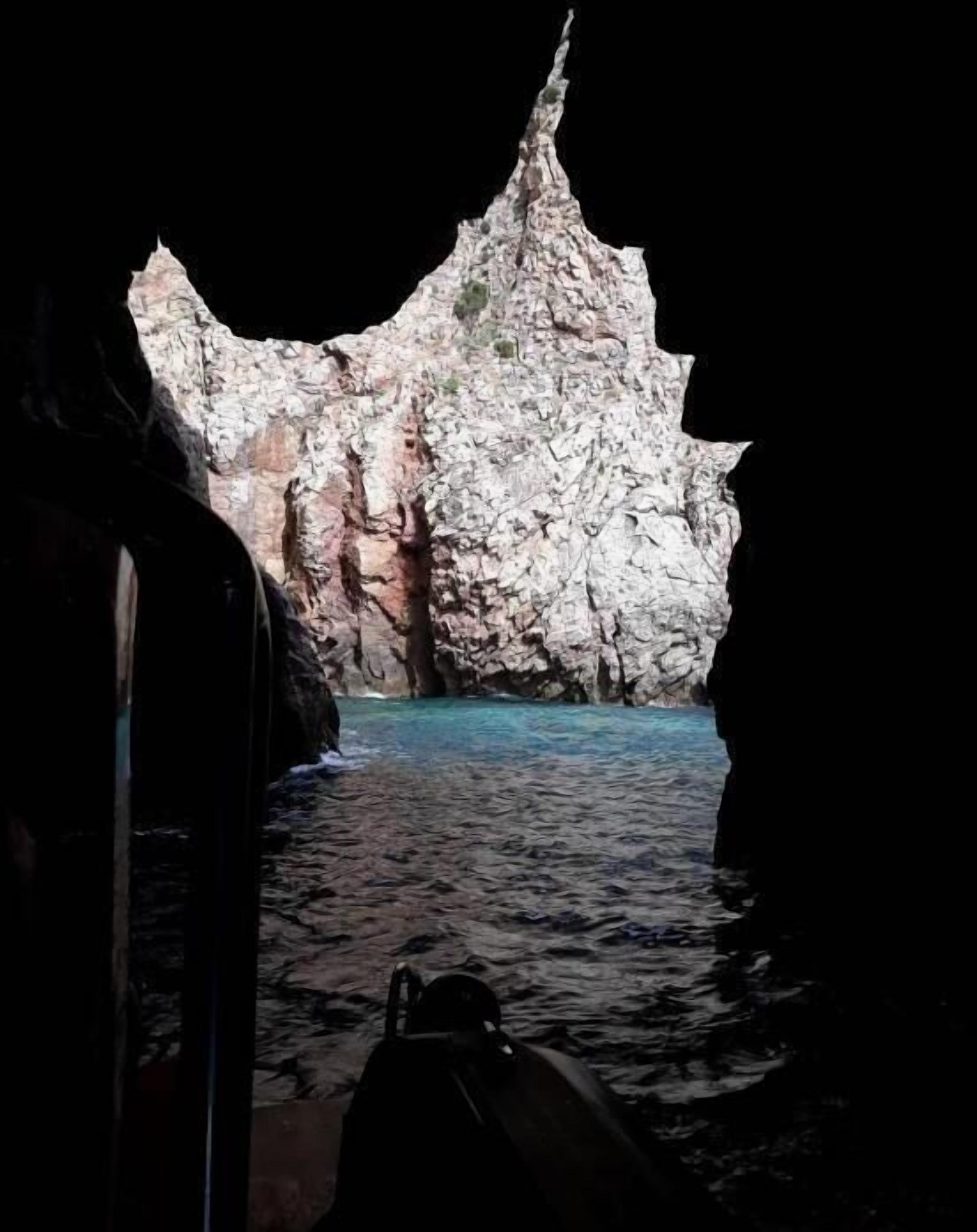 A rocky coastal cave entrance with clear blue water.