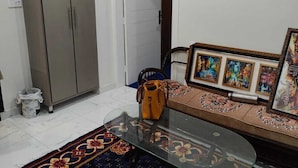 A living room with a glass coffee table, a sofa, a patterned rug, a wardrobe, and a door leading to another room.