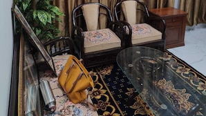 A living room with a sofa, two armchairs, a glass coffee table, a small wooden side table, a potted plant, and a patterned rug.