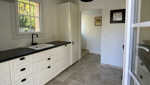 A modern kitchen with white cabinets, a black countertop, and a window with a view of greenery. - Au Calme, Très Jolie Maison, bel Espace Piscine, Pool House, Cadre Champêtre (Cadenet)