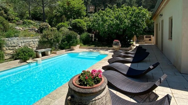 A swimming pool with lounge chairs and a stone planter with flowers. - Au Calme, Très Jolie Maison, bel Espace Piscine, Pool House, Cadre Champêtre (Cadenet)