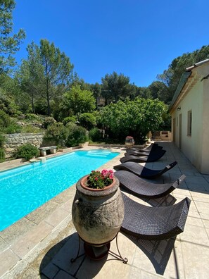 Una piscina con sillas de descanso y una jardinera de piedra con flores.