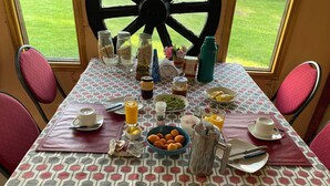 A breakfast table set with various food items and drinks, including cereal, juice, and pastries, with a view of a green lawn through a large window. - Patagonia Bordelago (Río Ibáñez)