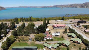 Vista aérea de una propiedad junto al lago, con varias construcciones, incluyendo una casa grande de techo rojo, varias cabañas más pequeñas y una instalación de paneles solares.