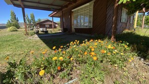 A rustic wooden house with a covered porch and a garden with yellow flowers. - Patagonia Bordelago (Río Ibáñez)