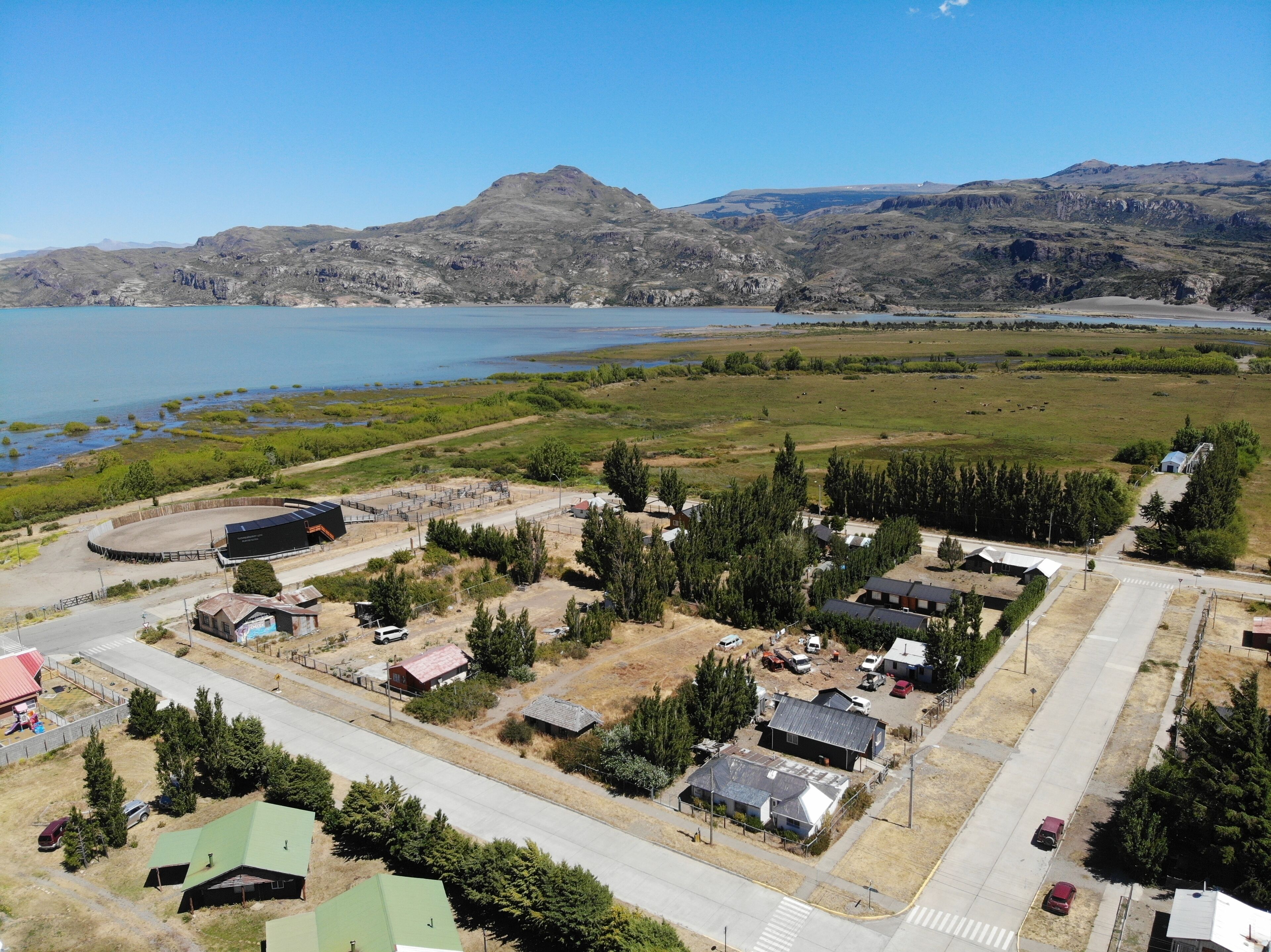 A rural area with a large body of water, mountains in the background, and a small settlement with several buildings and a road.