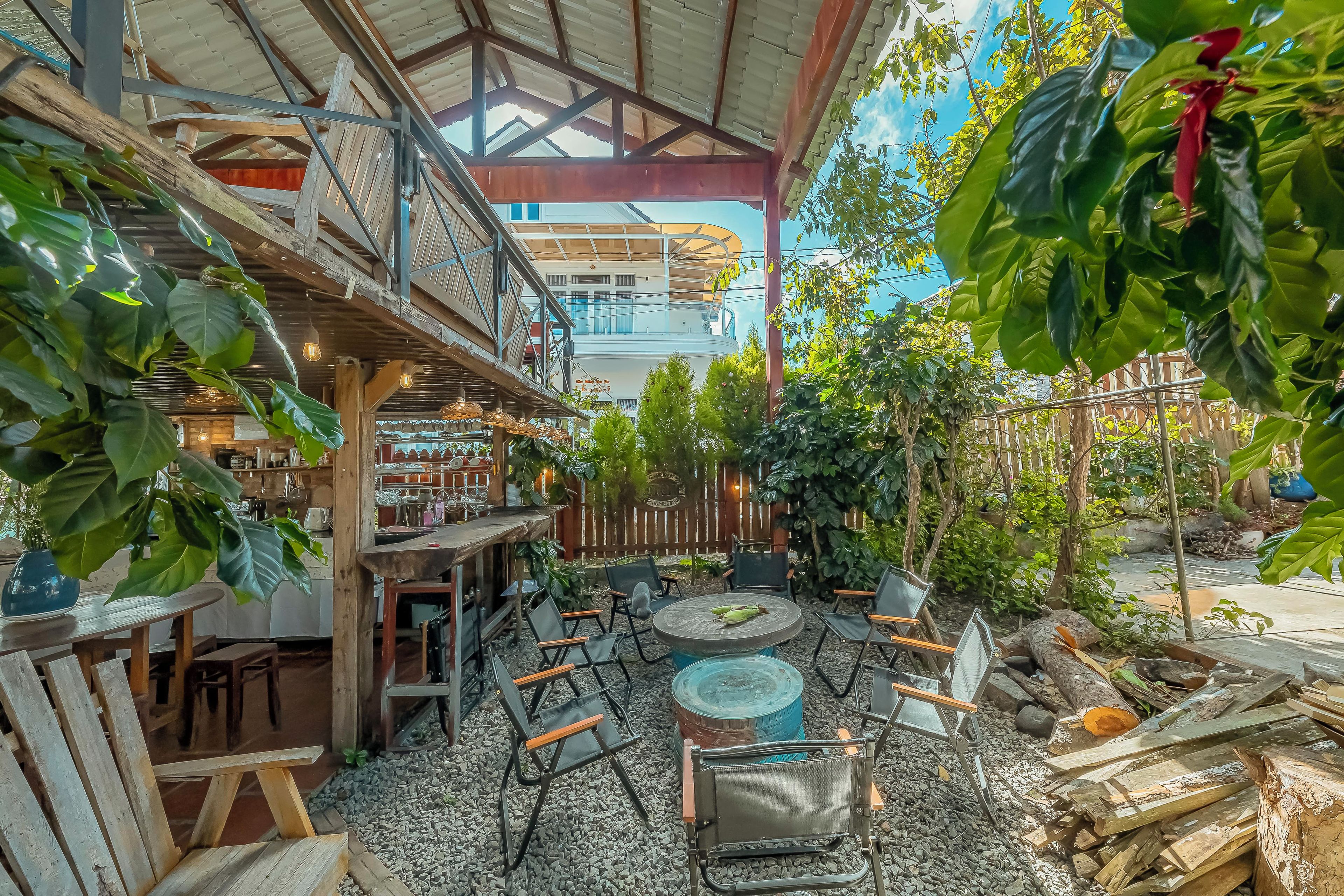 An outdoor seating area with tables and chairs, surrounded by greenery and a wooden deck.