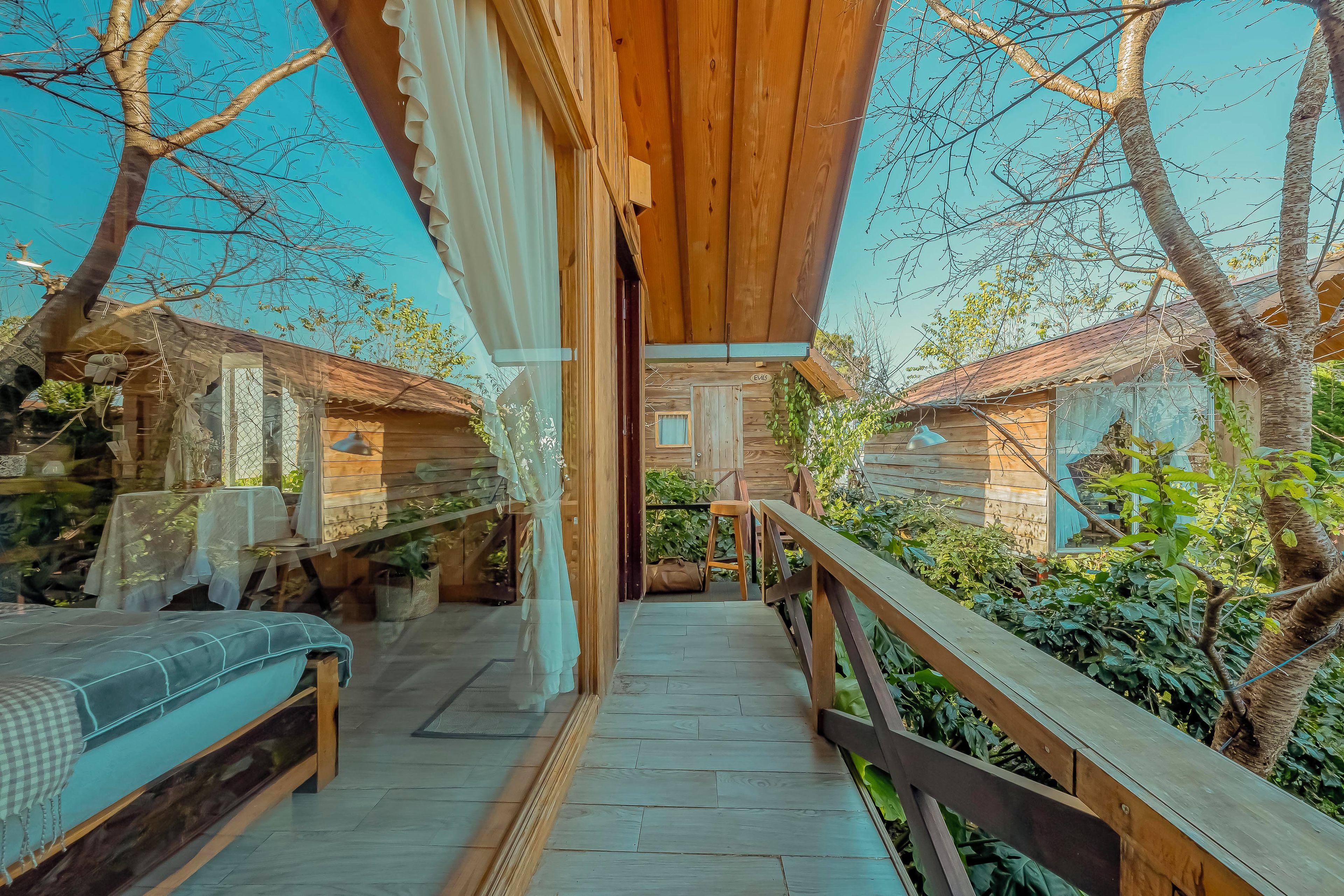 Una terraza de madera con un banco y una mesa, rodeada de follaje y árboles.