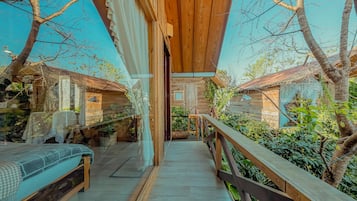 Una terraza de madera con un banco y una mesa, rodeada de follaje y árboles.