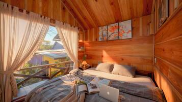 A wooden cabin bedroom with a bed, a laptop, and a window with curtains.