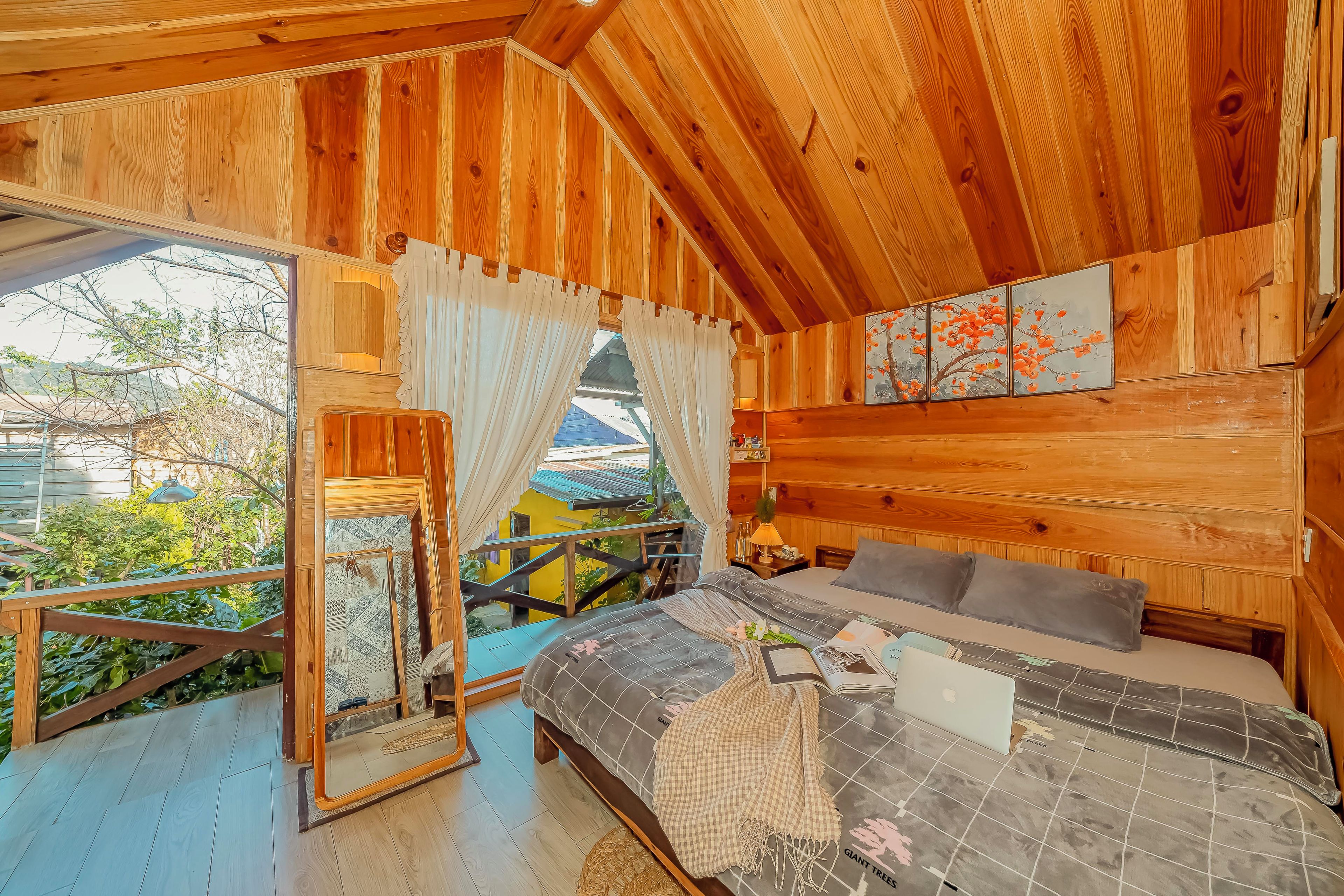 A wooden cabin with a bed, a small table, and a window overlooking greenery.