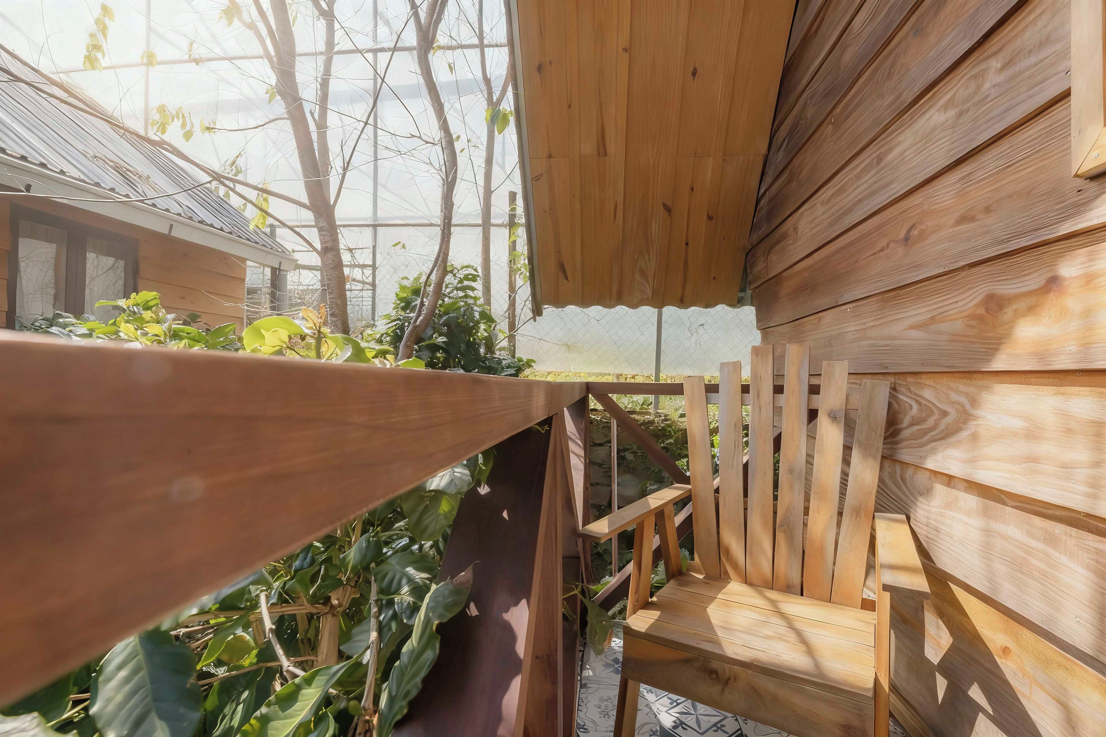 A wooden outdoor seating area with a table and chairs, surrounded by plants and a glass enclosure.