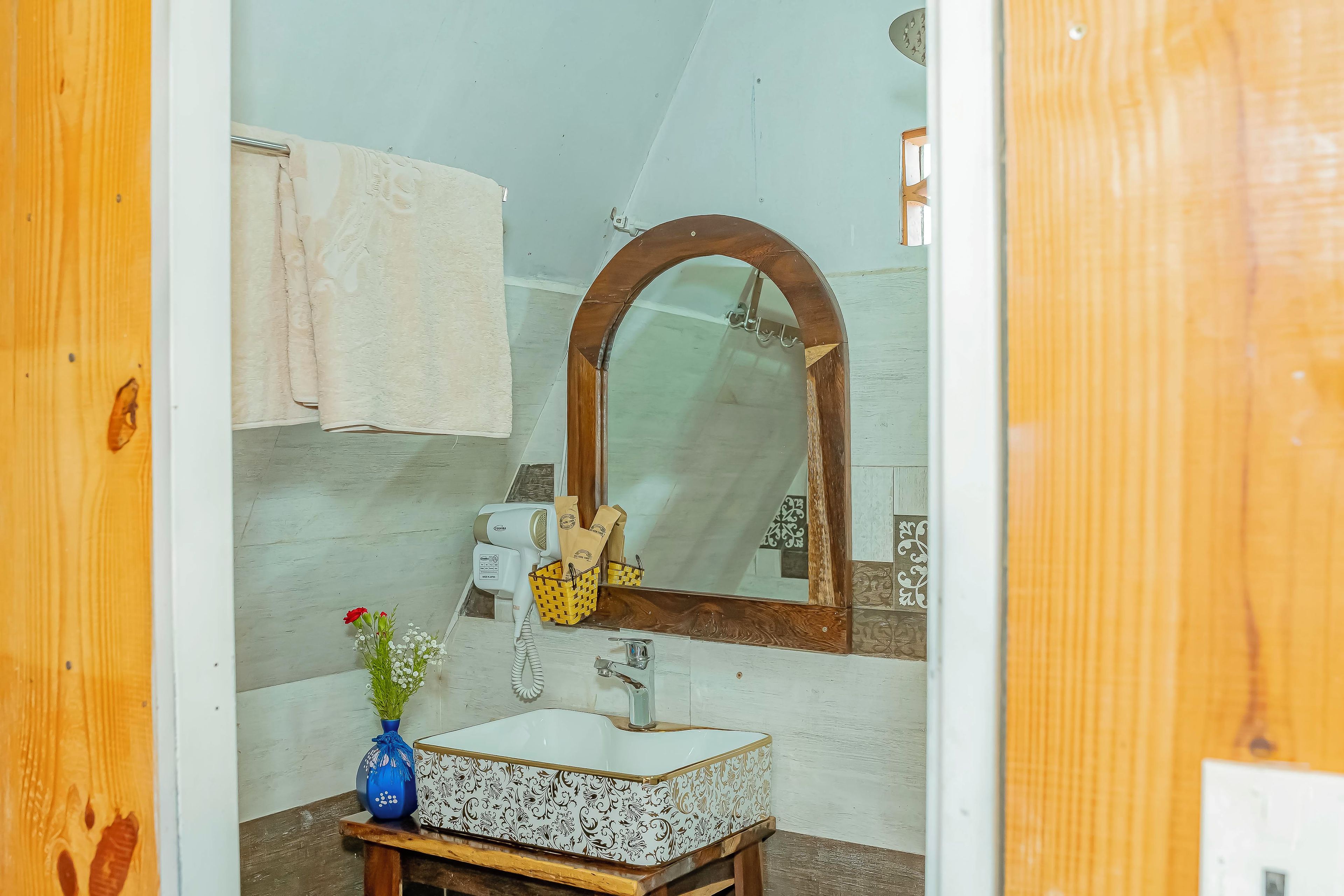 Ein Badezimmer mit einem weißen Waschbecken, einem Spiegel mit Holzrahmen, einem Handtuch auf einem Wäscheständer und einem Föhn an der Wand.