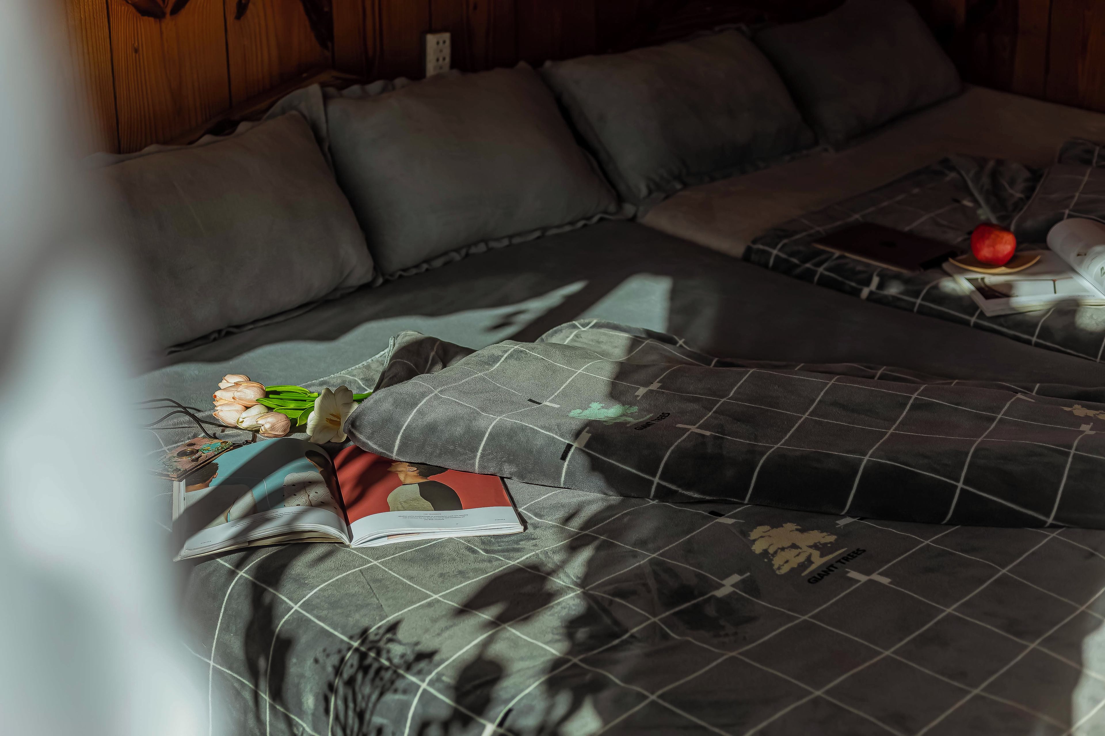 A room with a sofa, pillows, a book, a red apple, and a bouquet of flowers.