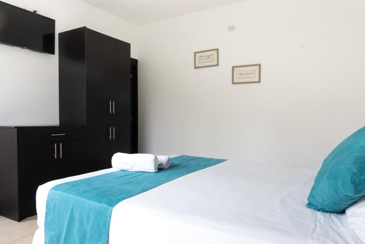 A hotel room with a bed, a black wardrobe, and two framed signs on the wall.