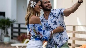 Una pareja se toma un selfie junto a una piscina, con un edificio blanco al fondo.