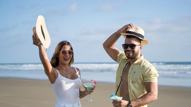 Una pareja en la playa sosteniendo bebidas y un sombrero.