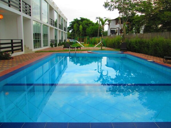 Una piscina con un borde de baldosas, rodeada por una cerca y vegetación.