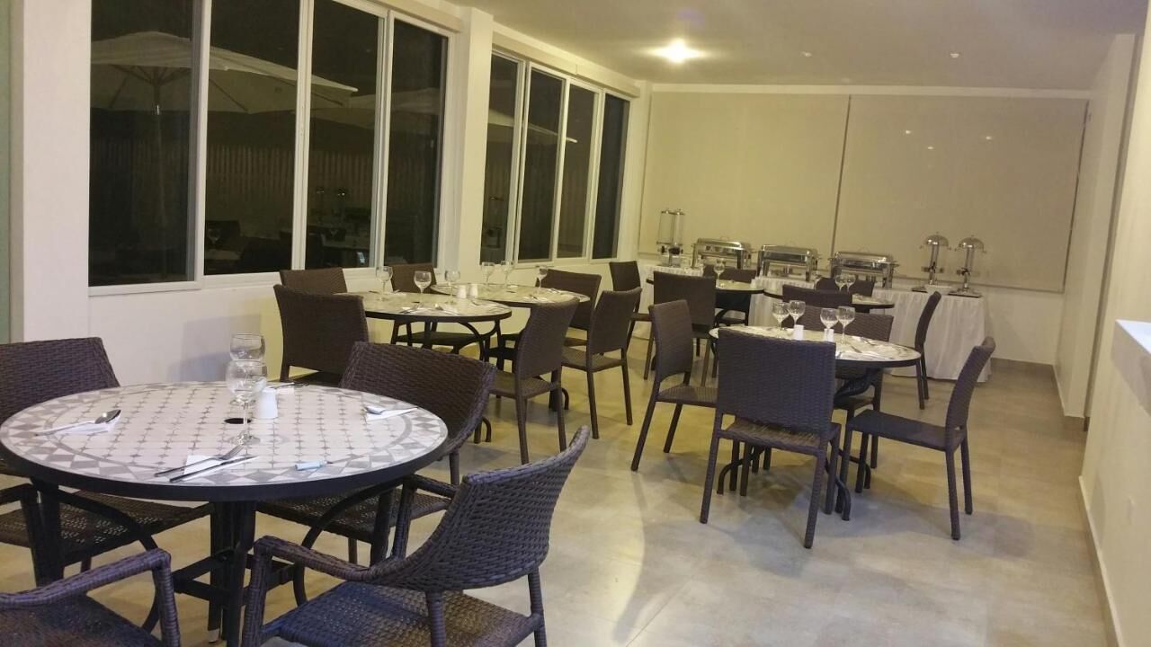 A dining area with round tables and chairs, large windows, and a kitchen in the background.