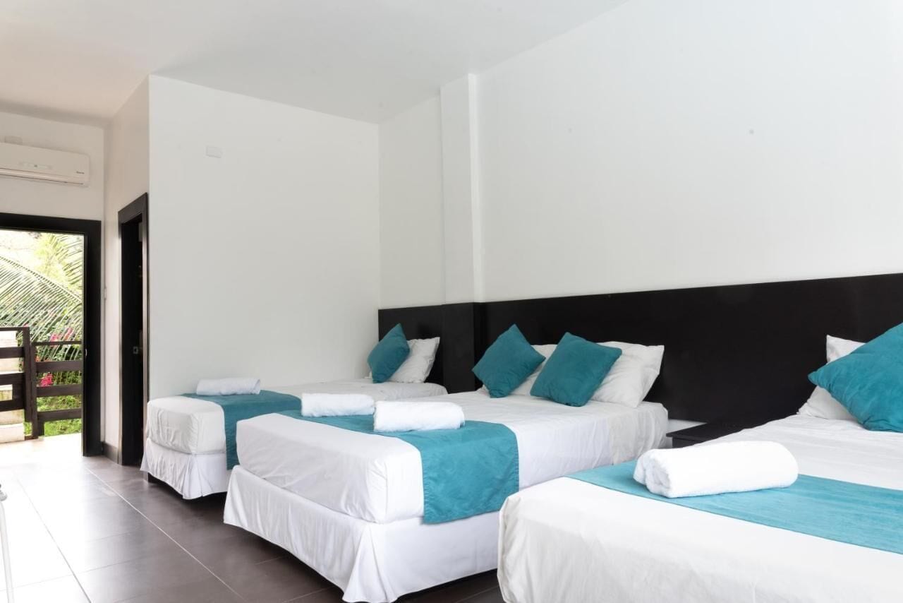 Habitación de hotel con tres camas, cada una con ropa de cama blanca y detalles en color aguamarina.