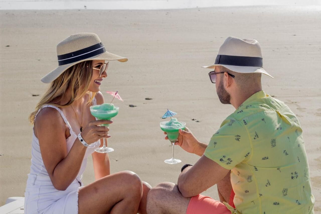 Twee mensen zitten op het strand, ieder met een drankje met rietje.
