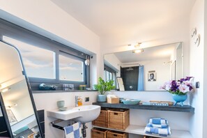 Une salle de bain moderne avec un grand miroir, un lavabo, une fenêtre et une étagère contenant des articles de toilette.