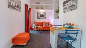 A compact living space with a sofa, a small table, and a chair. There are two artworks on the walls and a plant on the right. - Purgatorio Terrace - One Bedroom Apartment, Sleeps 2 (Naples)