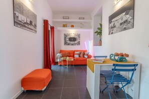 A living room with a sofa, a dining table with chairs, a red curtain, and a wall with a picture.