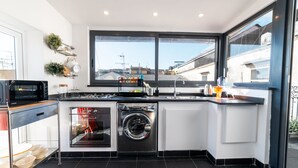 A modern kitchen with a built-in washer and dryer, large windows, and a view of the cityscape. - Purgatorio Terrace - One Bedroom Apartment, Sleeps 2 (Naples)