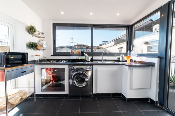 Une cuisine moderne dotée d’un lave-linge et d’un sèche-linge intégrés, de grandes fenêtres et offrant une vue sur le paysage urbain.
