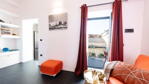 A modern living room with a sofa, a small table with decorative items, a bookshelf, and a view through a glass door. - Purgatorio Terrace - One Bedroom Apartment, Sleeps 2 (Naples)