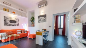 A modern living room with a sofa, a small table, and a chair. There is a dining area with a table and chairs. The room has a large window with curtains. - Purgatorio Terrace - One Bedroom Apartment, Sleeps 2 (Naples)