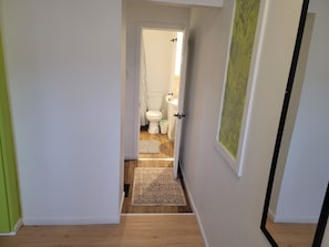 Kapea käytävä johtaa kylpyhuoneeseen, jossa on wc, pesuallas ja suihkuverho.