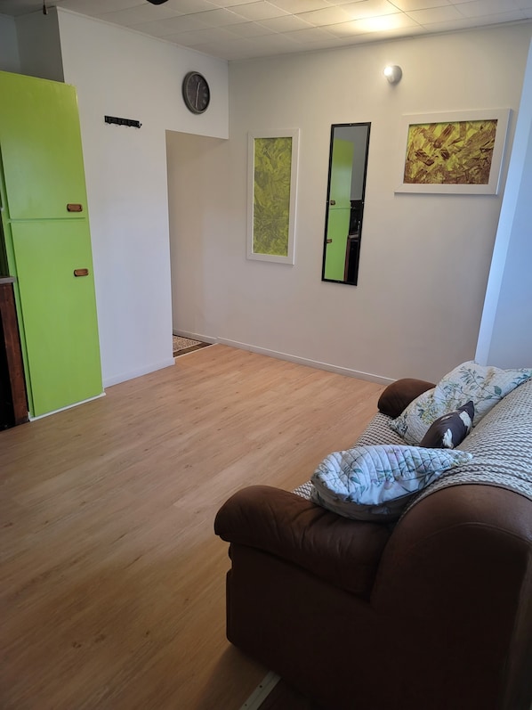 Ein Zimmer mit einem braunen Sofa, einem grünen Schrank, einer Uhr und zwei gerahmten Bildern an der Wand.