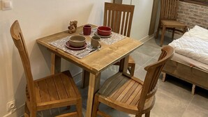 A small, cozy room with a wooden dining table set for two, a single bed, and a TV mounted on the wall.