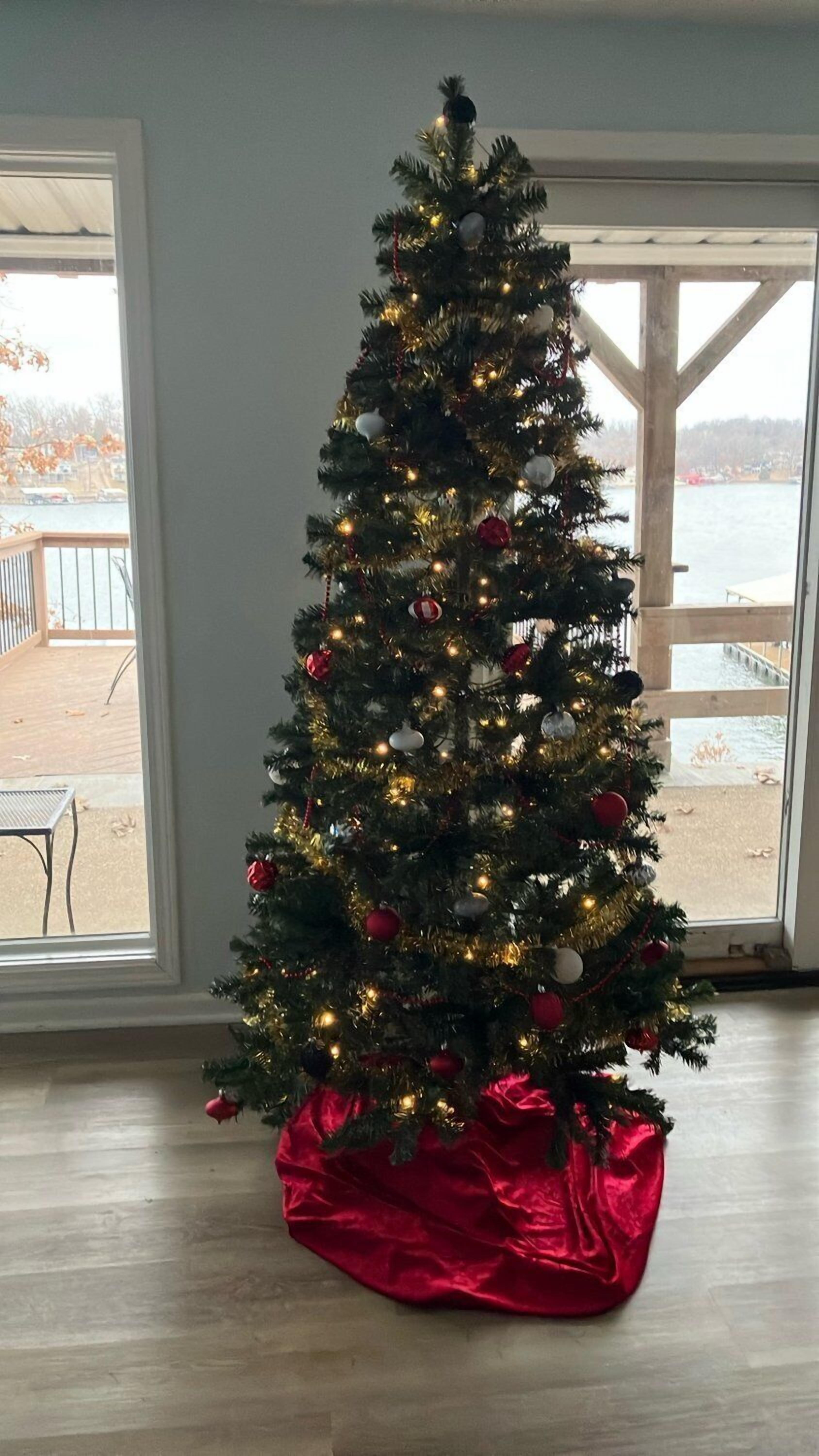 Un árbol de Navidad con luces y adornos en una habitación con ventanas grandes.