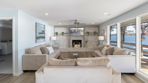 A modern living room with a fireplace, two sofas, a coffee table, and large windows overlooking a body of water.