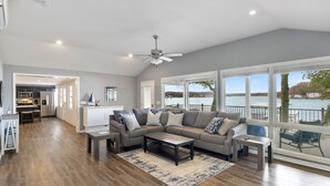 A spacious living room with a large gray sectional sofa, a coffee table, and a view of a lake through large windows. - Sunset & Lake Views, Kayak, Outdoor Dining & Seats (Gravois Mills)