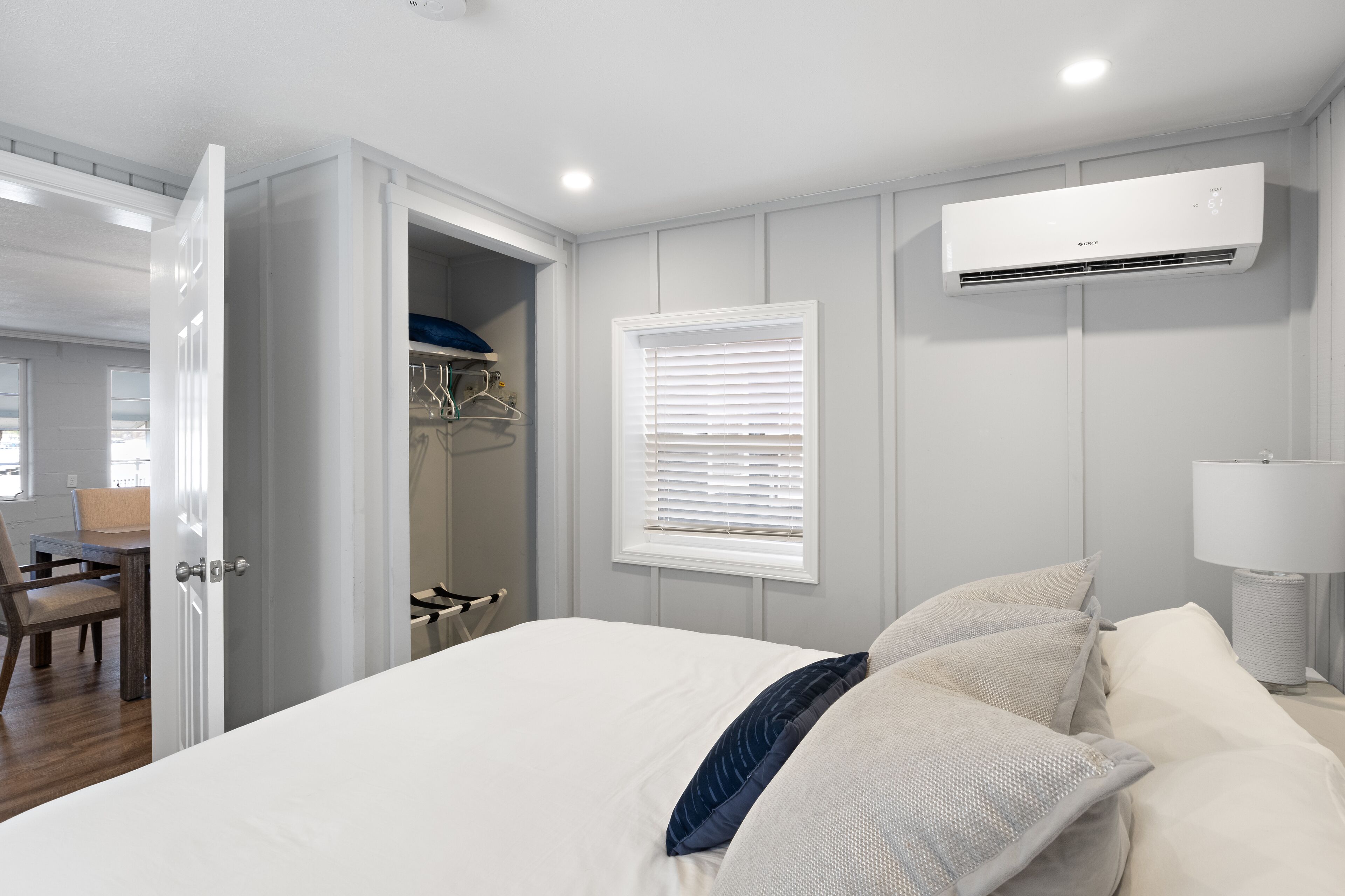 Een slaapkamer met een bed, een kledingkast, een raam met jaloezieën, een airconditioning en een lamp.