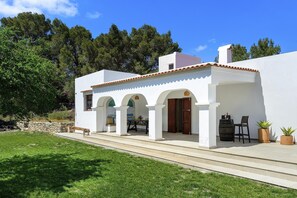 Un edificio blanco con techo de tejas, un patio con mesa y sillas, y una pared de piedra.