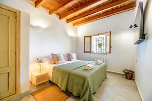 A bedroom with a wooden ceiling, a bed with green bedding, a bedside table with a lamp, a window with a view of greenery, and a potted plant. - Villa Can Rafalet - Five Bedroom Villa, Sleeps 10 (Ibiza)