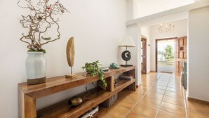 A hallway with a wooden console table, a vase with branches, a lamp, and a view to the outside. - New! Villa Can Jaume Arabí de Baix (Puig d'en Valls)