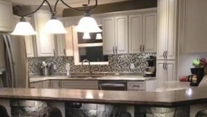 A kitchen with white cabinets, a stone accent wall, and three pendant lights.