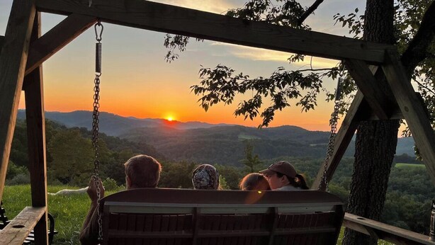 A wooden swing bench overlooking a sunset with a view of distant hills.