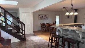 A spacious kitchen with a central island, wooden chairs, and a staircase leading to another level.